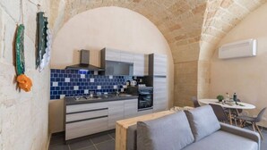 A compact kitchen with a modern design, featuring a built-in stove, a microwave, and a sink. There is a dining area with a round table and chairs, and a sofa. The kitchen has a stone archway and a tiled backsplash. - Balbo 7 Apartment - Lecce Selection (Lecce)