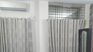 A bedroom with a single bed, a wardrobe, and a window with metal bars. - Hotel Charu (Barisal)