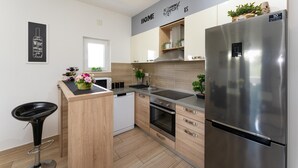 Una cocina moderna con refrigerador de acero inoxidable, armarios de madera, horno empotrado y un taburete negro.