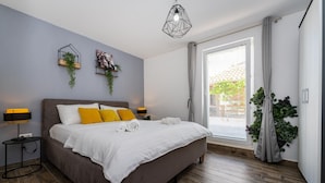 Un dormitorio moderno con una cama grande, dos mesitas de noche, una lámpara de diseño geométrico y vistas al exterior a través de una ventana.