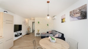 Un espacio de estar moderno con zona de comedor, sofá, televisor y aire acondicionado instalado en la pared.