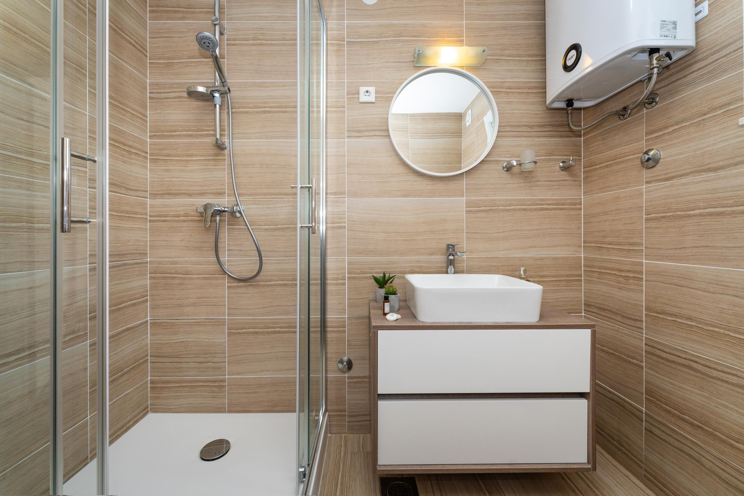 A modern bathroom with a glass shower enclosure, a white sink, and a mirror.