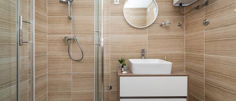 A modern bathroom with a glass shower enclosure, a white sink, and a mirror.