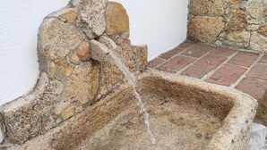 Une fontaine en pierre au design rustique, placée devant un mur blanc et sur un sol en briques.