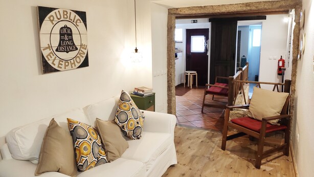 Un salon chaleureux avec un canapé blanc, des coussins à motifs, une chaise en bois et un panneau indiquant « TÉLÉPHONE PUBLIC » sur le mur.