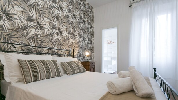 A neatly made bed with striped pillows, a wooden headboard, and a window with sheer curtains. - ⭐ The Colosseum Mansion ⭐ (Roma)