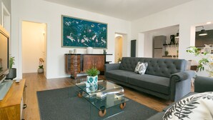 A modern living room with a glass coffee table, grey sofa, and a large tropical-themed painting. - ⭐ The Colosseum Mansion ⭐ (Roma)