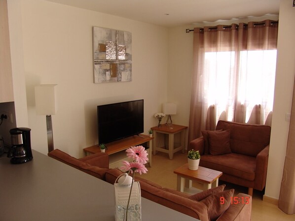 A modern living room with a flat-screen TV, a sofa, a coffee table, and a small side table.