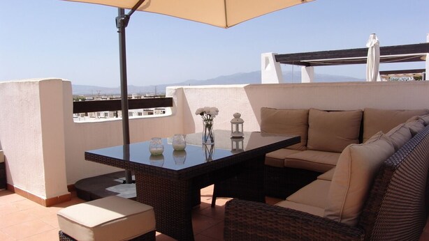 A terrace with a table, chairs, and a sofa under a large umbrella.