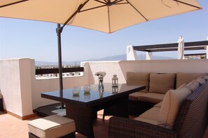 A terrace with a table, chairs, and a sofa under a large umbrella.