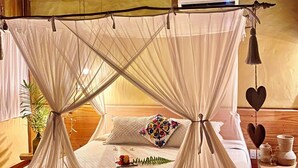 A room with a bed under a canopy, wooden beams on the ceiling, and a bedside table with decorative items. - Casa das Rendas Exclusive Bungalows (Amontada)
