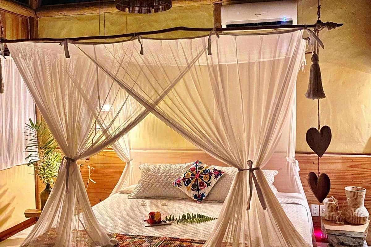A room with a bed under a canopy, wooden beams on the ceiling, and a bedside table with decorative items.