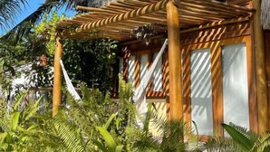 A thatched-roof structure with a wooden pergola, surrounded by lush tropical vegetation. - Casa das Rendas Exclusive Bungalows (Amontada)