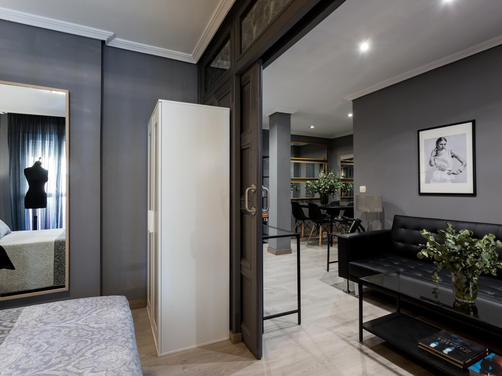 Un dormitorio moderno con cama, armario, zona de comedor con mesa y sillas, y sala de estar con sofá y planta.