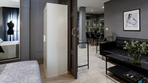 A modern bedroom with a bed, a wardrobe, a dining area with a table and chairs, and a living area with a sofa and a plant. - Holi-Rent Gran Poder (Sevilla)