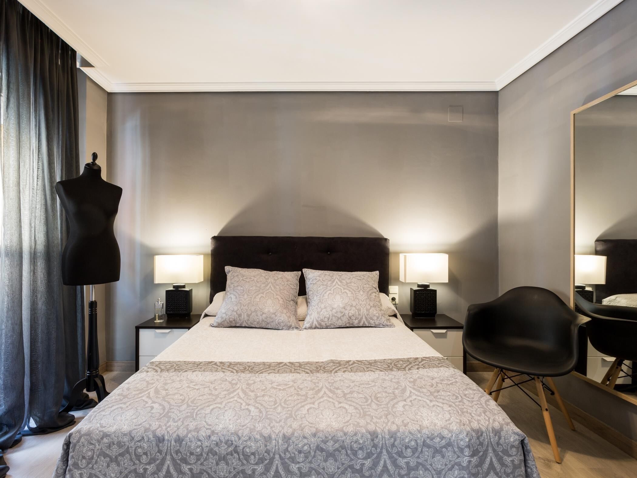 A modern hotel room with a large bed, two bedside lamps, a black chair, and a mannequin.