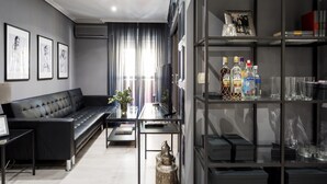 A modern living room with a black leather sofa, a glass coffee table, and a bookshelf containing various items. - Holi-Rent Gran Poder (Sevilla)