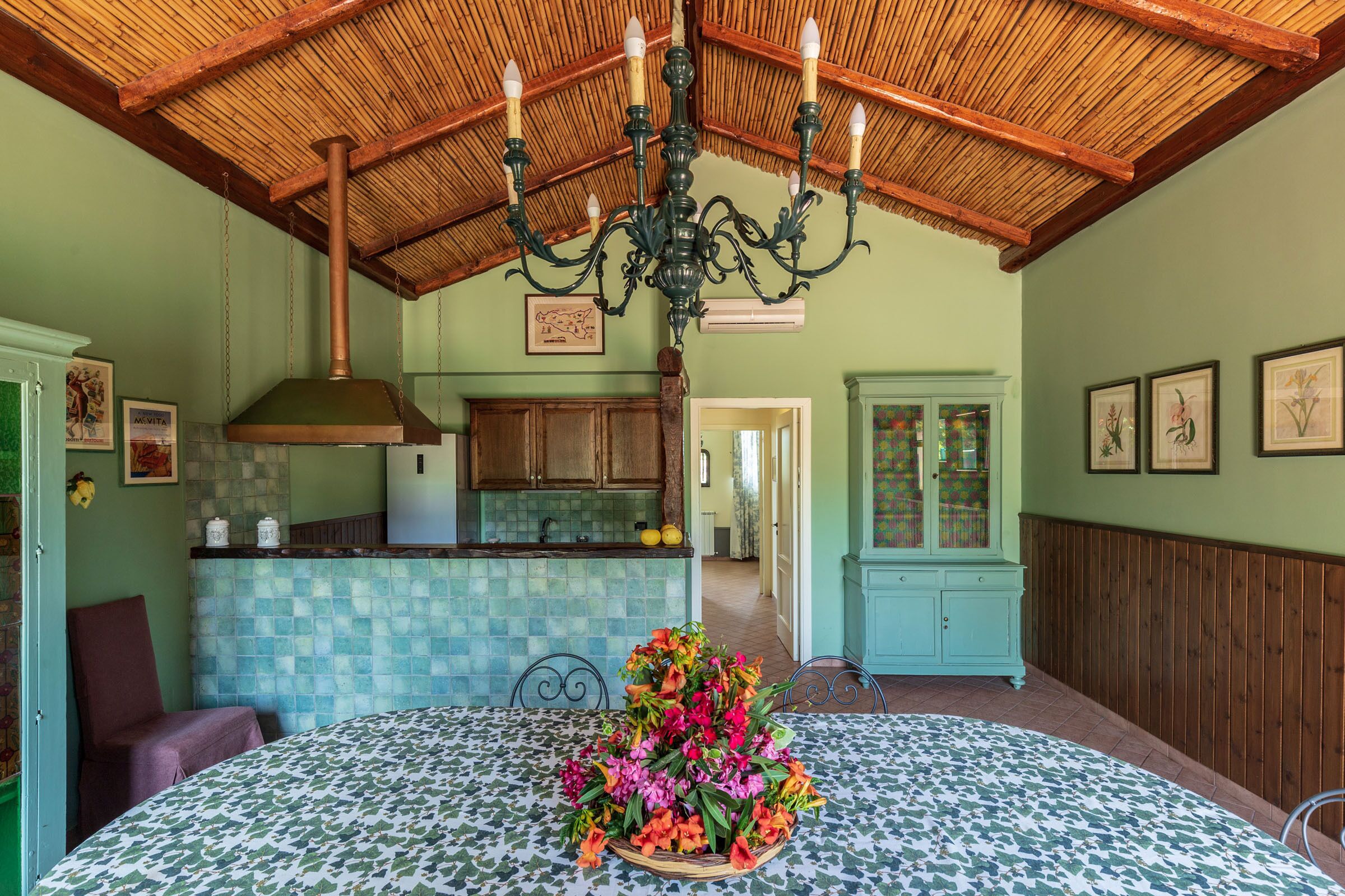 A dining area with a patterned tablecloth, a floral centerpiece, and a wooden ceiling.
