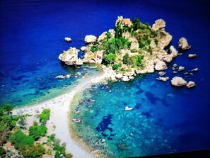 An aerial view of a coastal area with rocky terrain, clear blue waters, and a small beach with umbrellas.