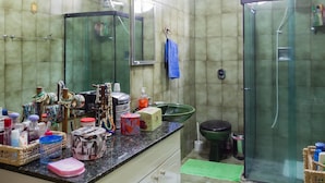 Een badkamer met een douchecabine van glas, een wastafel met een groene kom en diverse toiletartikelen op het aanrecht.