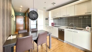 A modern kitchen with white cabinets, a stainless steel sink, and a microwave. There is a dining area with a wooden table and chairs. - Apartment in front of Fira Gran Via (Hospitalet de Llobregat - Barcelona)