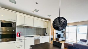 A modern kitchen with white cabinets, stainless steel appliances, and a wooden dining table. - Apartment in front of Fira Gran Via (Hospitalet de Llobregat - Barcelona)