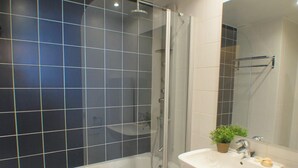 A modern bathroom with a glass-enclosed shower, a white sink, and a mirror. - Apartment in front of Fira Gran Via (Hospitalet de Llobregat - Barcelona)