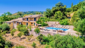 En villa med swimmingpool, omgivet af frodig vegetation og bakker.