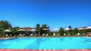 A swimming pool with lounge chairs and umbrellas, surrounded by trees and a building.