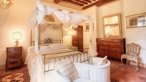 A bedroom with a four-poster bed, a wooden dresser, a chair, and a mirror.
