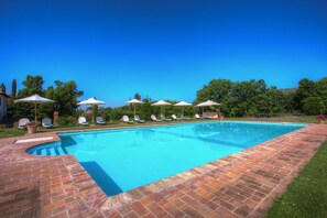 Una piscina rettangolare con bordo in mattoni, circondata da sedie a sdraio e ombrelloni.