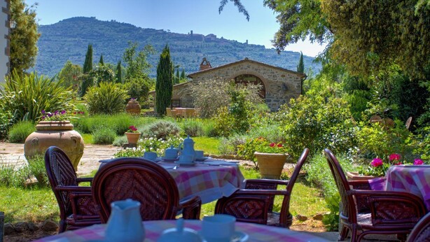 A garden patio with a stone building, outdoor seating, and a view of a hill.