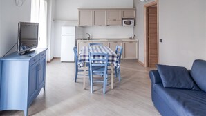 Ett kompakt bostadsutrymme med en matplats, ett litet kök och en tv som står på ett skåp.