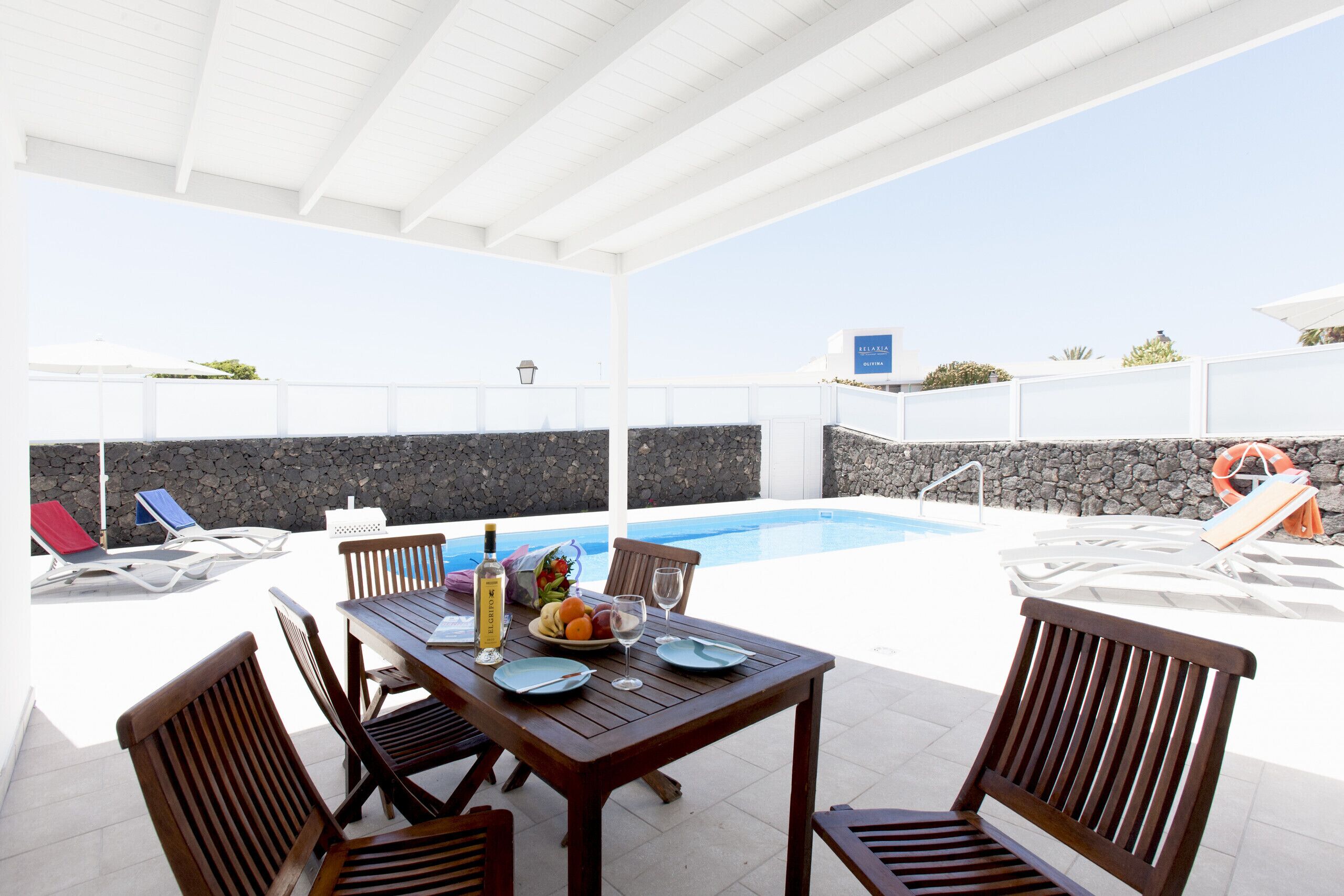 Un patio al aire libre con piscina, mobiliario de madera y un muro de piedra.