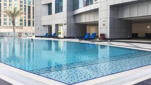 Ein moderner Hotelpoolbereich mit klarem, blauem Pool, blauen Liegestühlen und einem mehrstöckigen Gebäude im Hintergrund.