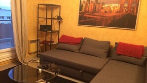 A living room with a sofa, a coffee table, a bookshelf, and a cityscape painting on the wall. - 70m2 apartment in the district of the barracks of Bonne (Grenoble)