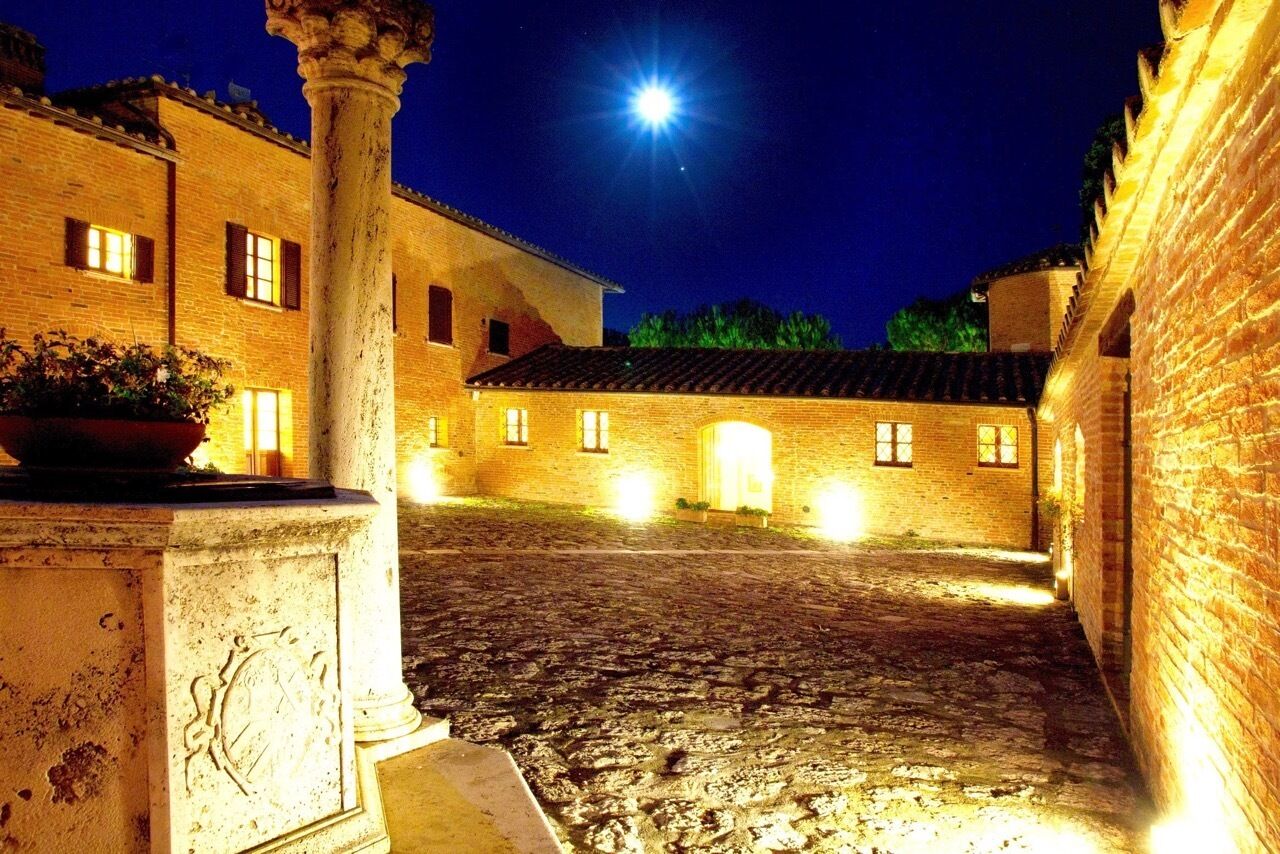 Ein Innenhof mit Kopfsteinpflaster, einer großen Säule und einem Gebäude mit beleuchteten Fenstern bei Nacht.
