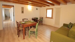 Zona pranzo con tavolo e sedie in legno, un divano verde e una finestra con persiane.