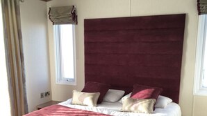 A bedroom with a large bed, a wooden nightstand, and a window with curtains.
