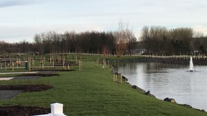 A park with a pond, grassy areas, and a wooden fence.