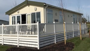 A single-story mobile home with a white exterior, a covered porch, and a fenced yard.