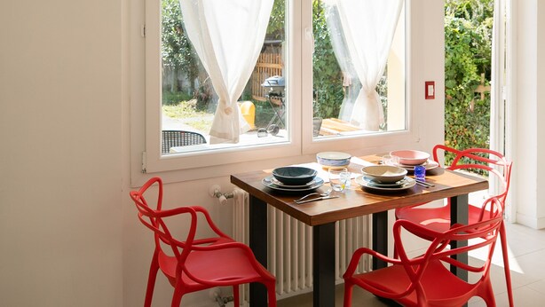 Un espace repas comprenant une table, des chaises et une vue sur le jardin grâce à de grandes fenêtres.