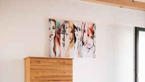 Une chambre avec une commode en bois, un lit et un grand tableau abstrait accroché au mur.