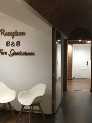 Zona de recepción con un cartel que dice 'Reception B&B Fiori Gianicolese' y dos sillas blancas con patas de madera.