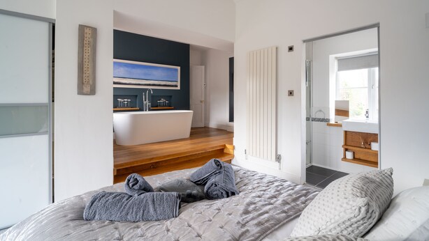 A modern bedroom with a large bed, a view of a bathroom, and a painting on the wall.