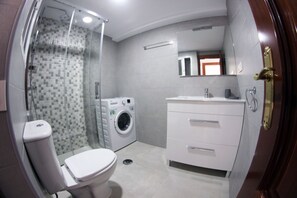 Un bagno con doccia in vetro, lavatrice, WC e una cassettiera.