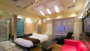 A hotel room with a bed, a desk, a red sofa, a TV, and a minibar. - HOTEL D-WAVE Shinjuku - Adults Only (Tokyo)