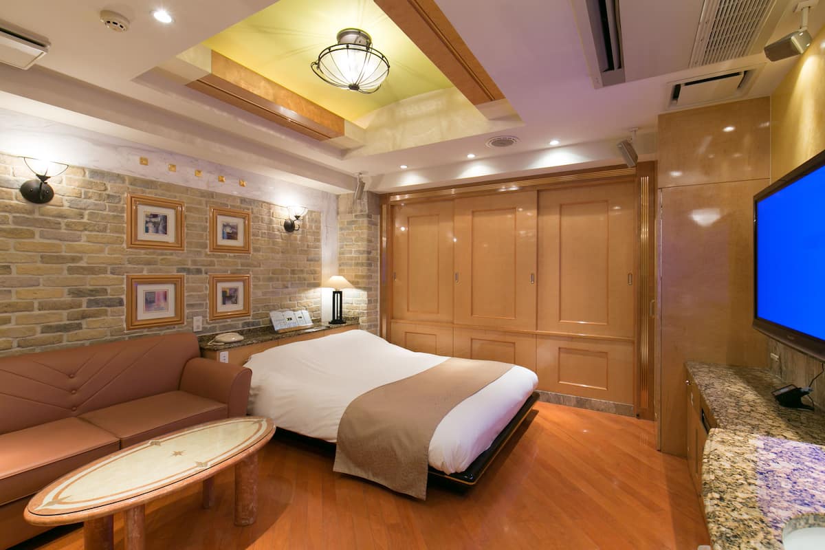 Une chambre d’hôtel avec un lit, un canapé, une télévision, une lampe et un mur en pierre orné de tableaux encadrés.