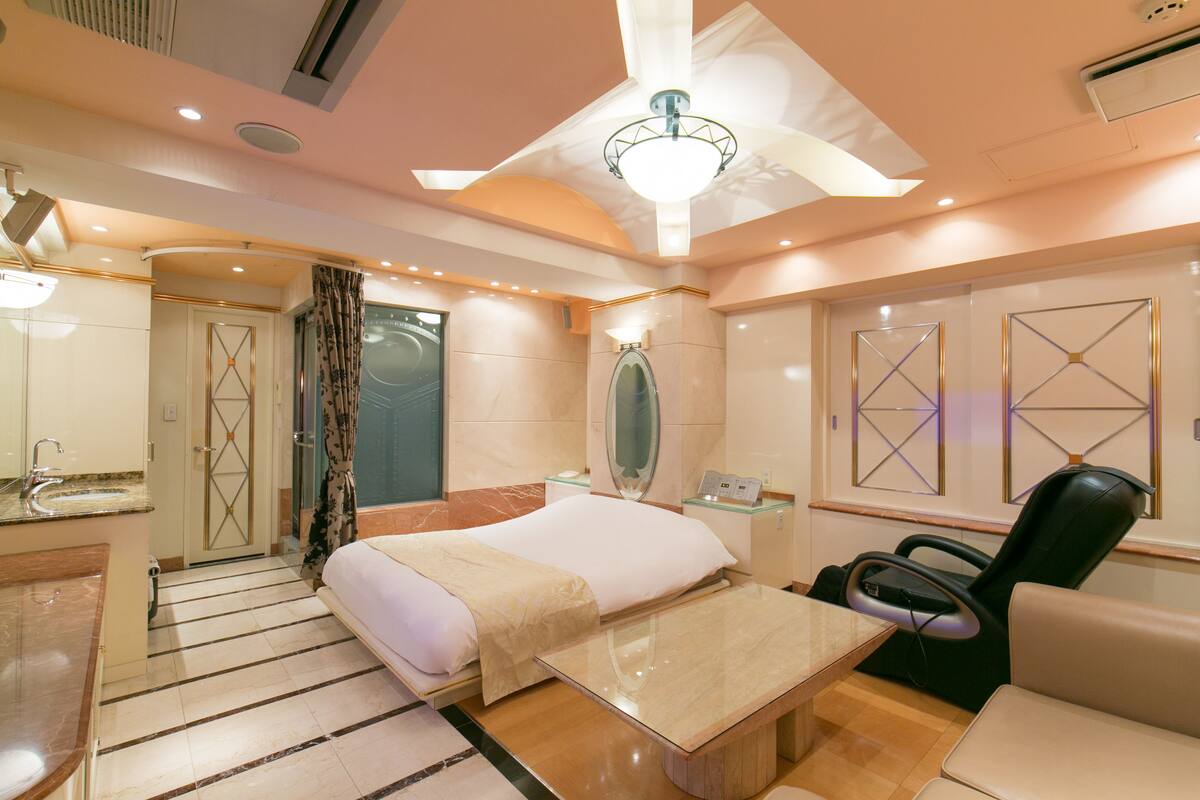 Une chambre d’hôtel moderne équipée d’un lit, d’un fauteuil massant, d’une coiffeuse avec miroir et d’un espace douche.
