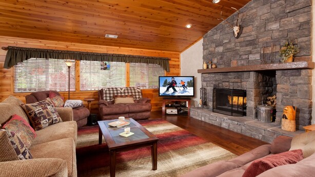 Una sala de estar acogedora con chimenea de piedra, techo de madera y un televisor que muestra una escena de esquí.